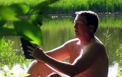 Man reading a book next to lake.