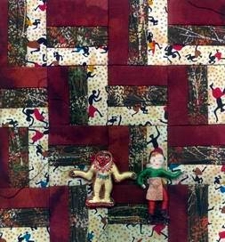 Log cabin quilt square with two dolls on it.